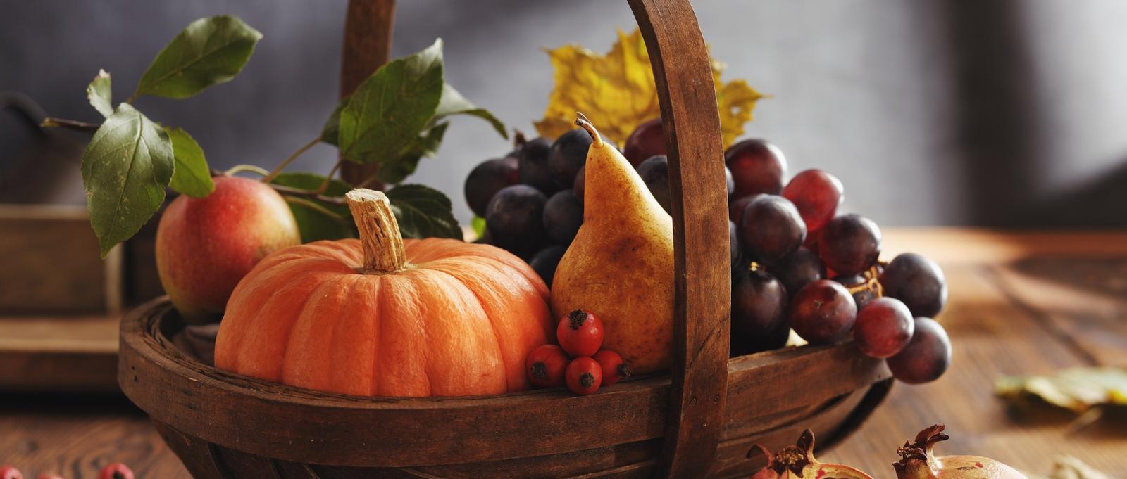 Panier en bois rempli de récoltes d'automne comprenant des citrouilles, des poires, des pommes, des raisins et des baies avec des feuilles d'automne.