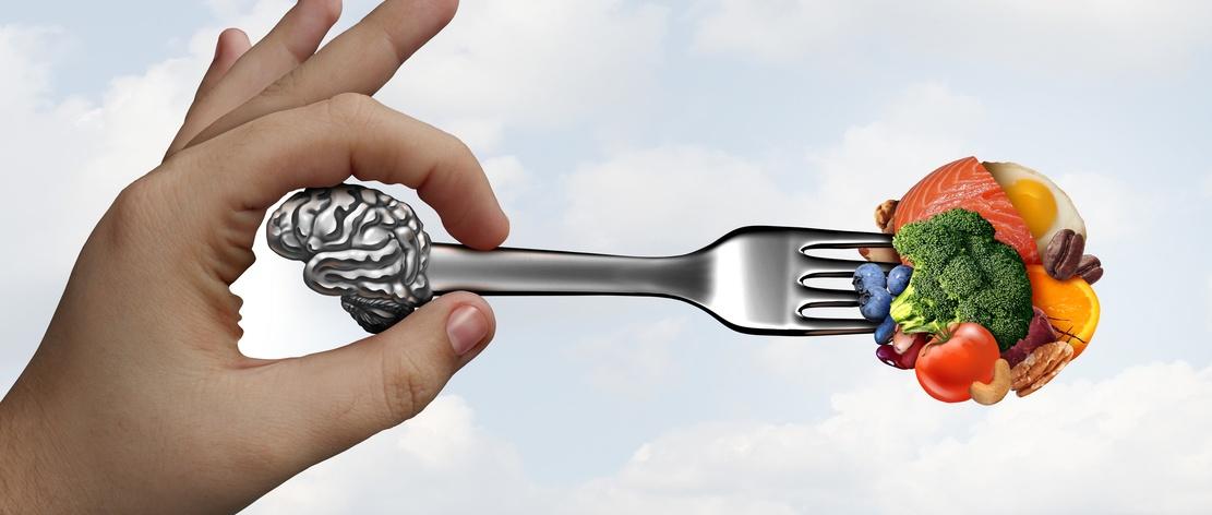 Hand holding fork with brain on one end and healthy foods on the other, symbolising brain nutrition connection.
