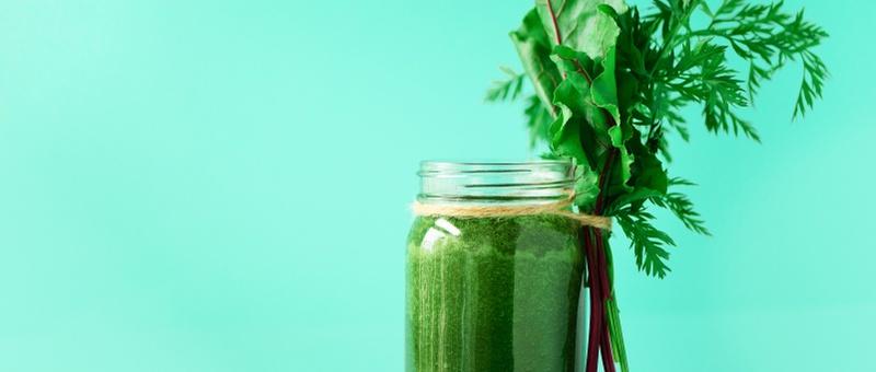 Glass jar filled with green smoothie drink with green vegetable garnish against a turquoise background.