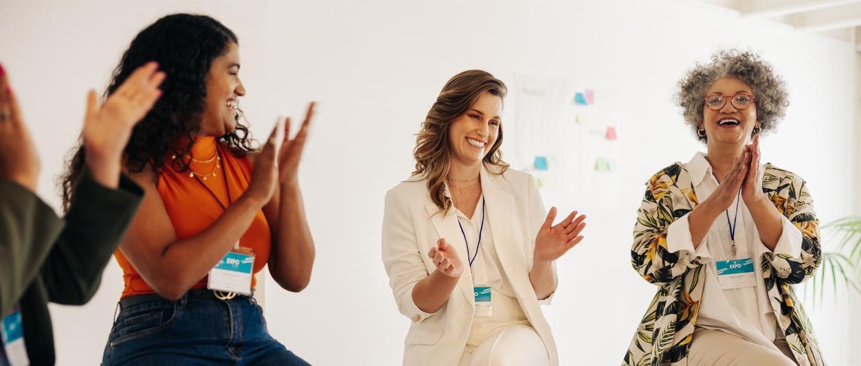 Photo de trois femmes portant des cordons d'employés et applaudissant lors d'une réunion