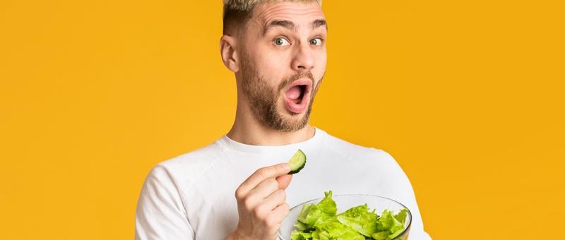 Homme en t-shirt blanc mangeant un saladier avec ses mains sur fond jaune.