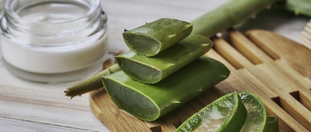 Tranches d'aloe vera et crème hydratante sur une table en bois.
