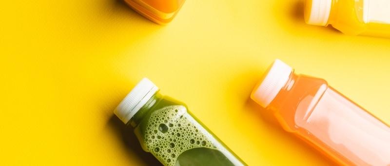 Jus de fruits colorés dans des bouteilles en plastique sur fond jaune.