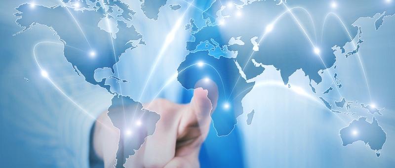 Main touchant une carte du monde numérique avec des lignes de connexion lumineuses reliant les continents sur un fond bleu.