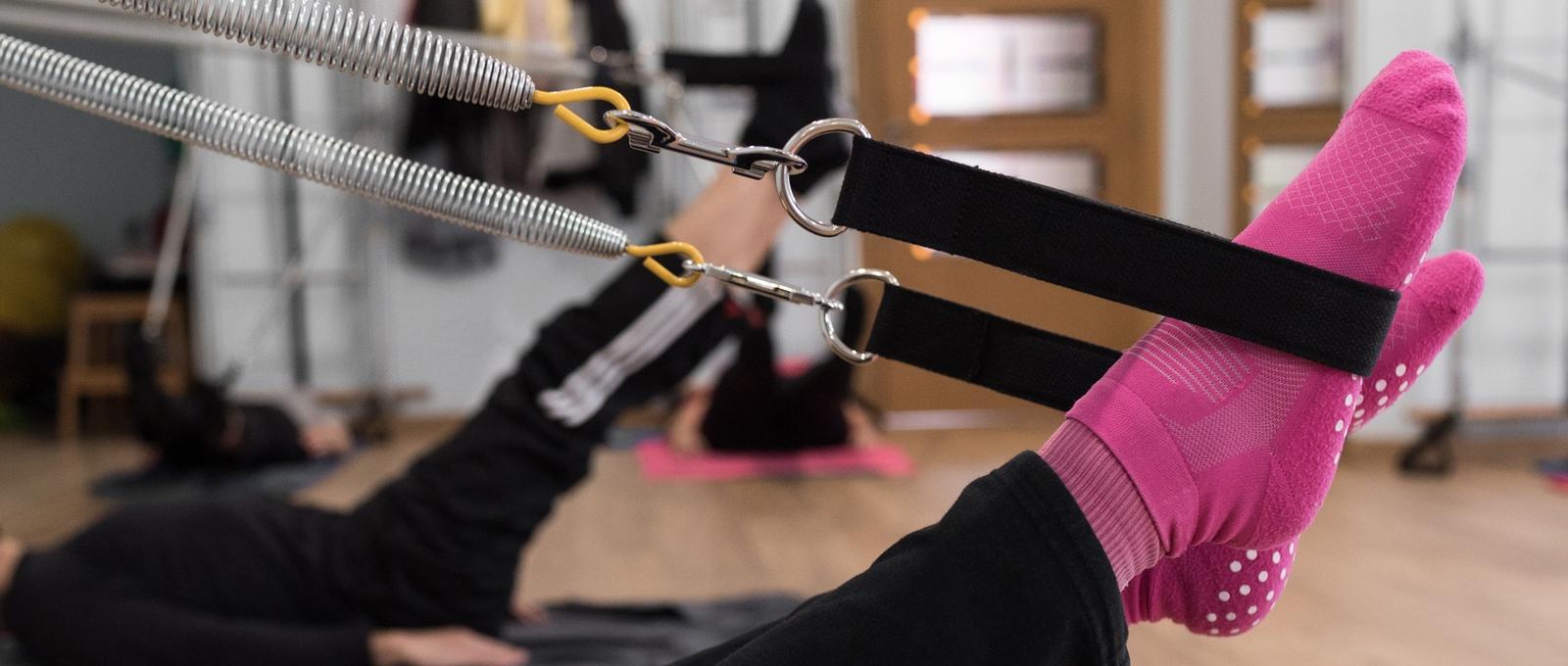 Femme anonyme en chaussettes claires levant les jambes et étirant les ressorts lors d'un entraînement de Pilates en groupe dans un studio.