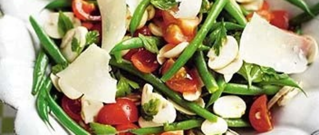 Salade de haricots verts frais avec tomates, copeaux de fromage et fines herbes, servie dans un bol blanc festonné sur un tissu à carreaux.
