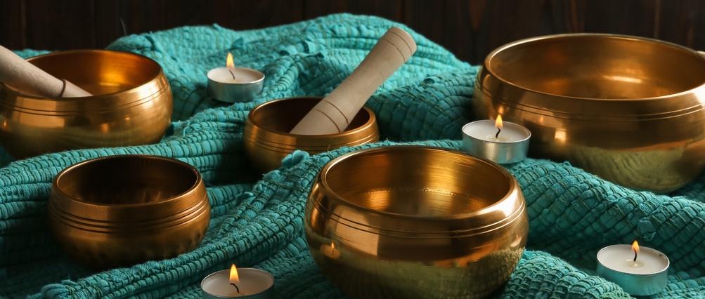 Bols chantants tibétains avec maillets, bougies allumées et tissu turquoise sur table en bois
