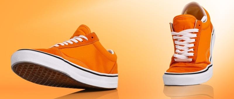 Disembodied orange and white trainers walking against orange background.