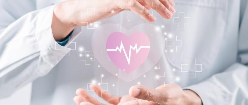 Les mains d'un professionnel de la santé entourent un coeur rose numérique avec une ligne de battements cardiaques, entouré de symboles médicaux en forme de croix.