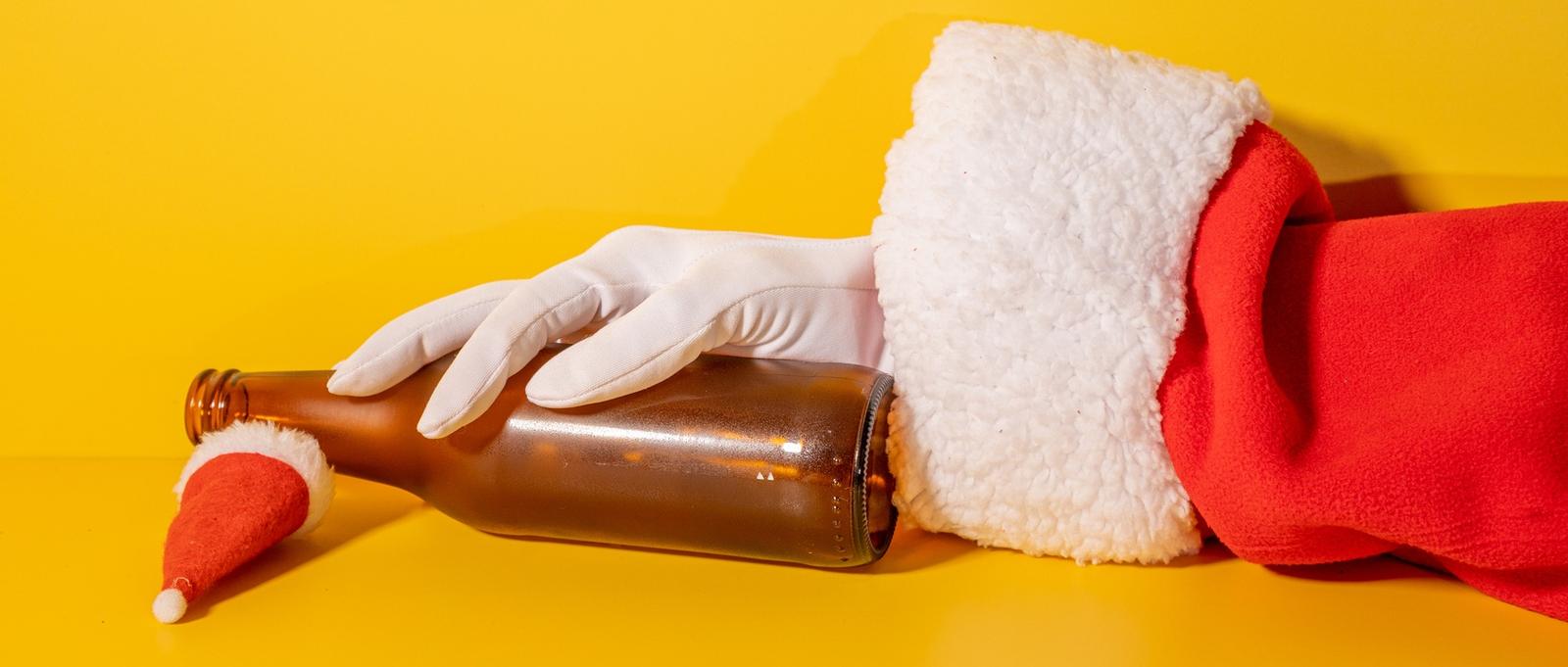 Père Noël tenant une bouteille de bière avec ses mains sur fond jaune