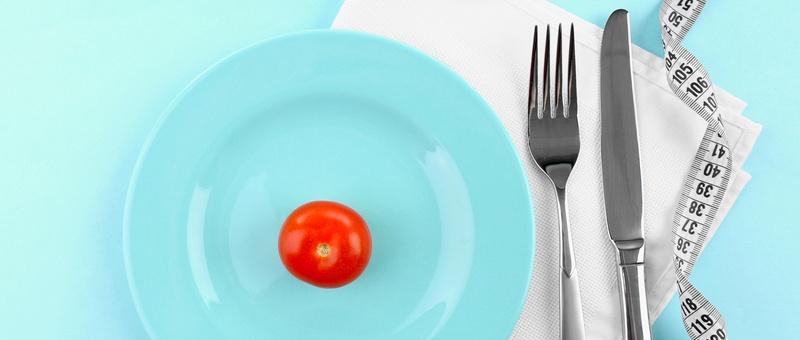 Tomate cerise rouge sur une assiette blanche à côté d'un mètre ruban et de couverts. Fond bleu.