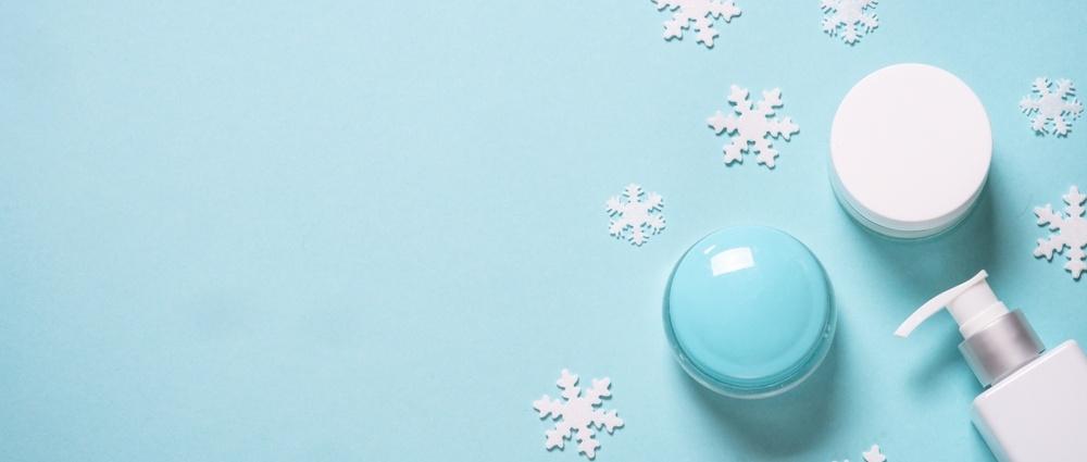 Assorted blue and white containers of skincare products surrounded by white snowflakes on a blue background.