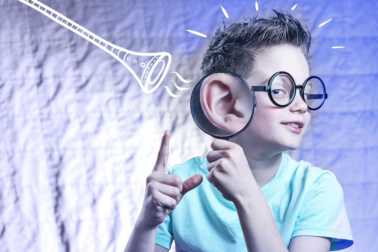 Enfant portant des lunettes rondes et tenant une loupe à l'oreille, avec des sons de trompette illustrés à proximité.