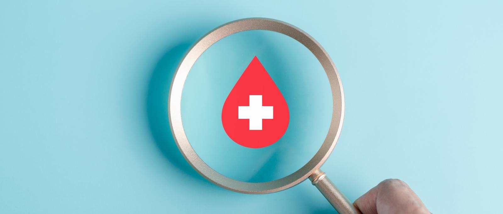 Main tenant une loupe et se concentrant sur l'icône d'une goutte de sang rouge sur fond bleu pâle.