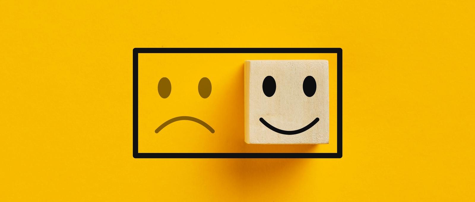 Deux cubes en bois avec l'icône de l'humeur joyeuse sur l'icône de l'humeur triste sur fond jaune