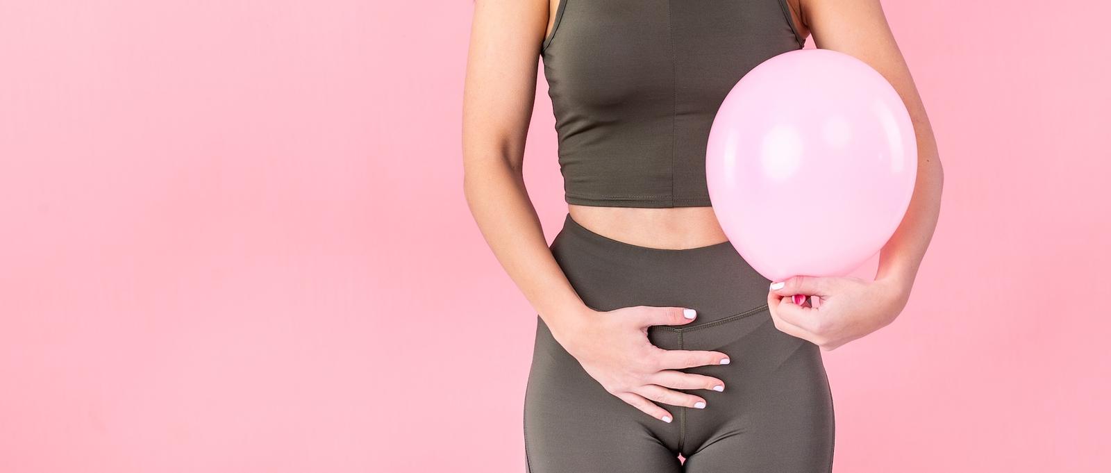 Gros plan d'une femme se tenant le ventre de la main droite et tenant un ballon rose dans la main gauche. L'image évoque une grossesse extra-utérine.