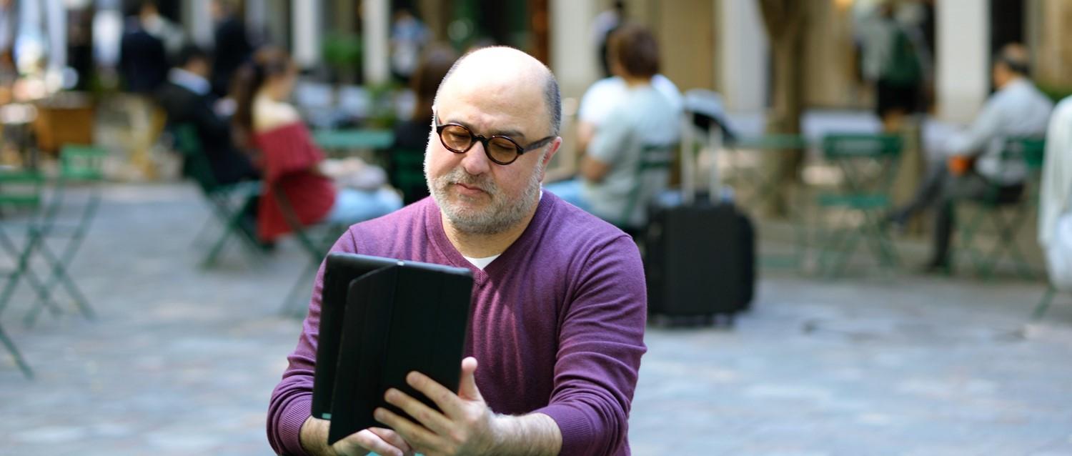 Bald man sitting outside reading tablet