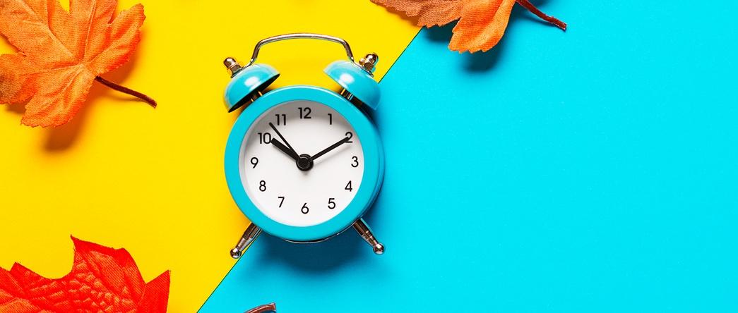 Horloge sur fond bicolore jaune et bleu clair décoré de feuilles mortes colorées.