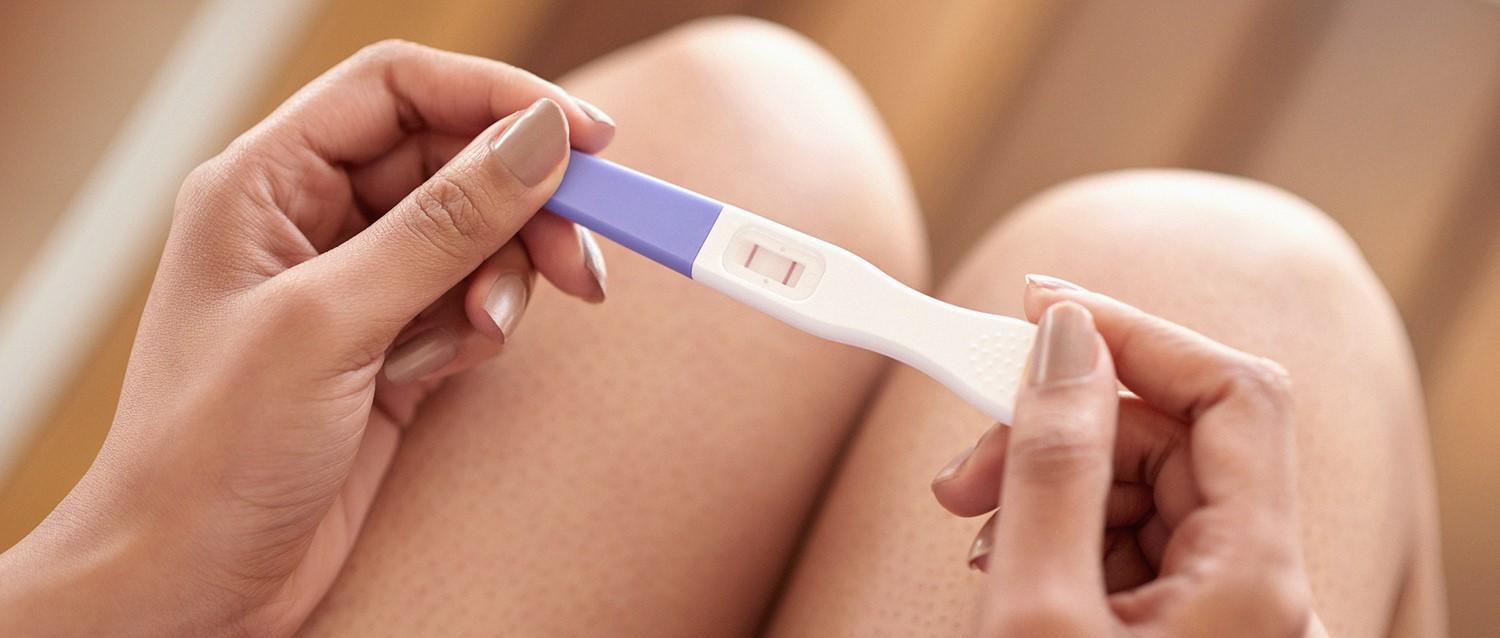Mains tenant un test de grossesse positif sur fond de ventre de femme enceinte.