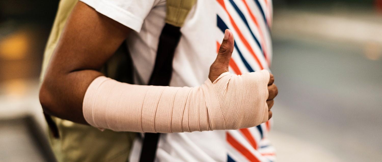 Personne portant une chemise blanche à rayures rouges et bleues montrant une main et un avant-bras enveloppés d'un bandage beige.