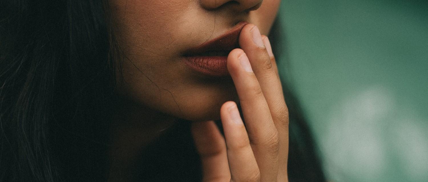 Gros plan d'une personne aux lèvres rouges se touchant le visage pensivement sur un fond vert tendre.