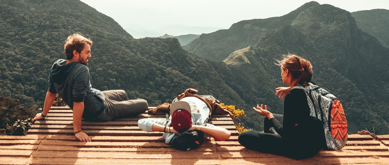 Randonneurs se reposant sur une plate-forme en bois surplombant un paysage de montagne spectaculaire avec des vallées verdoyantes et des sommets lointains.