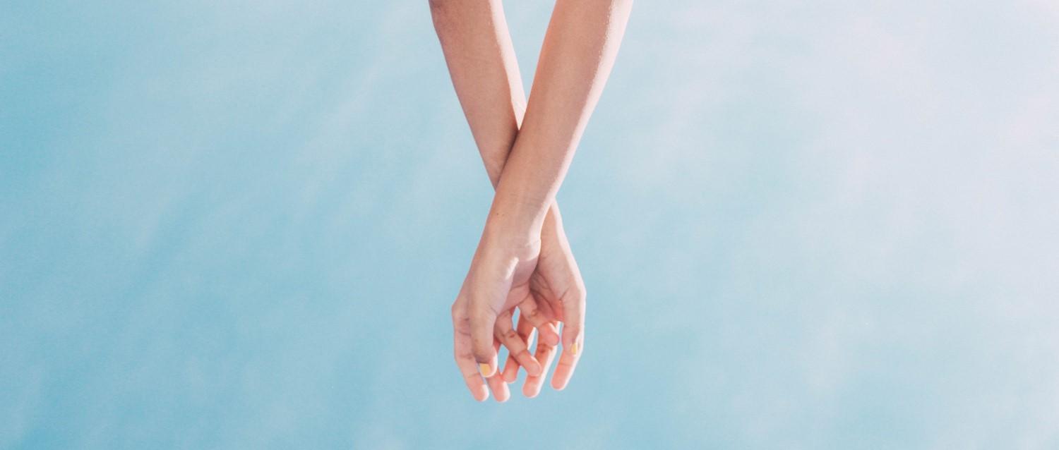 Deux mains se touchent doucement, les doigts entrelacés, sur un fond bleu clair, évoquant l'intimité et la connexion.