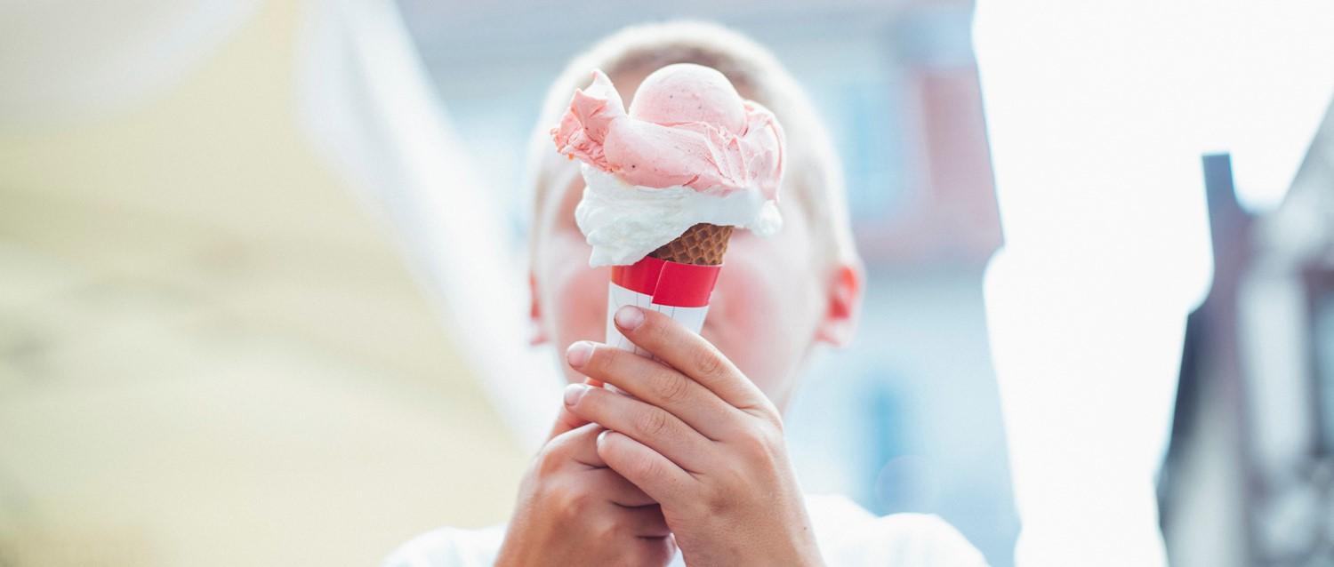 Mains tenant un cornet de glace à la fraise avec des boules roses et de la crème fouettée sur un fond clair et flou.