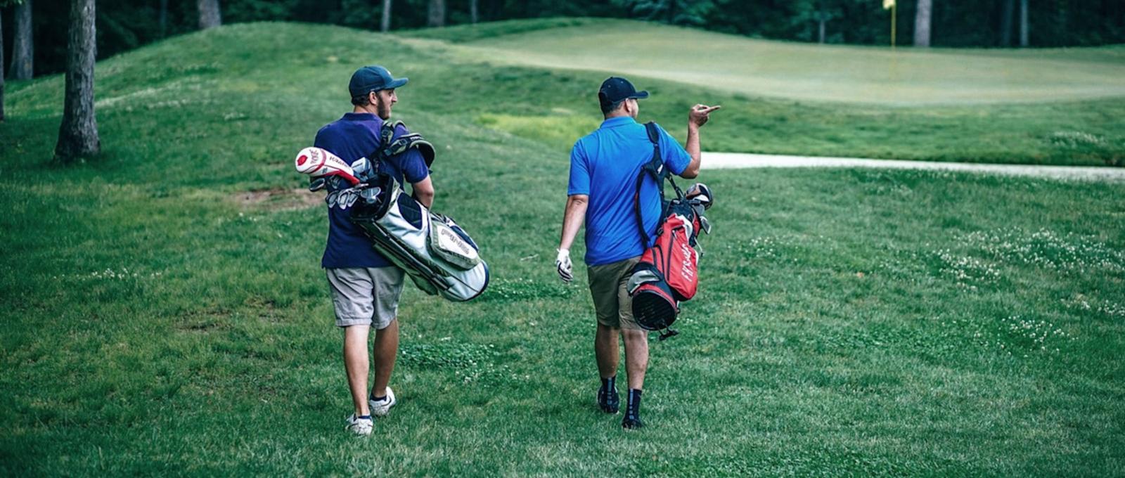 Deux golfeurs traversent un parcours vert en portant des sacs de golf, l'un argenté et l'autre rouge, en direction du trou suivant.