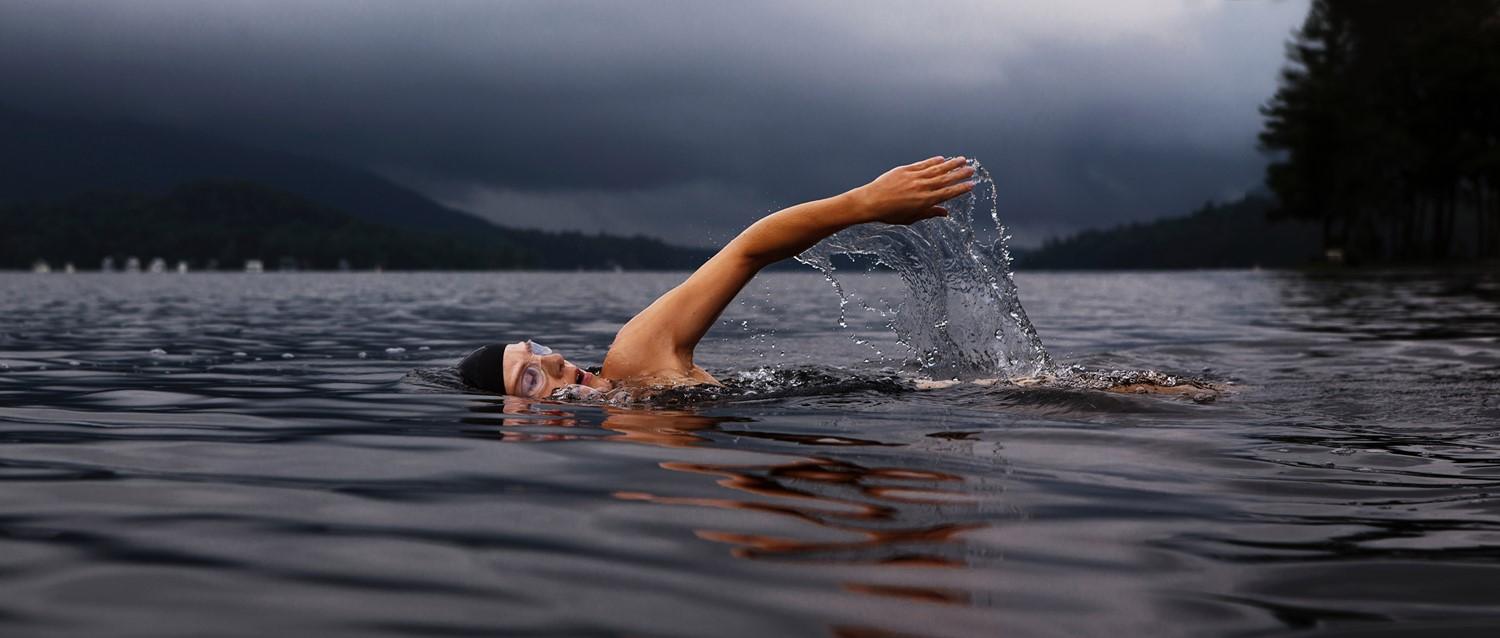 Nageur faisant du crawl avant dans un lac de montagne brumeux, les bras créant des éclaboussures sur fond de ciel d'orage sombre.