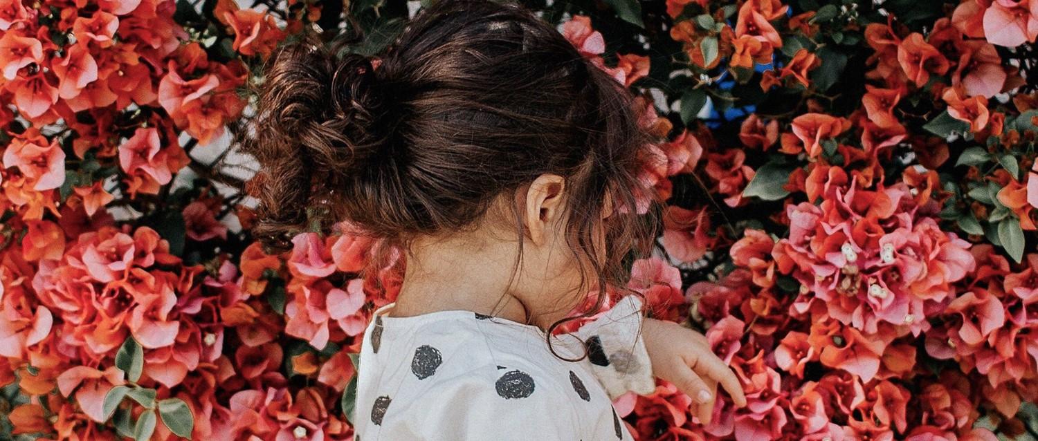 Personne aux cheveux bruns en chignon portant des vêtements à pois entourés de fleurs corail vibrantes et de feuilles vertes.