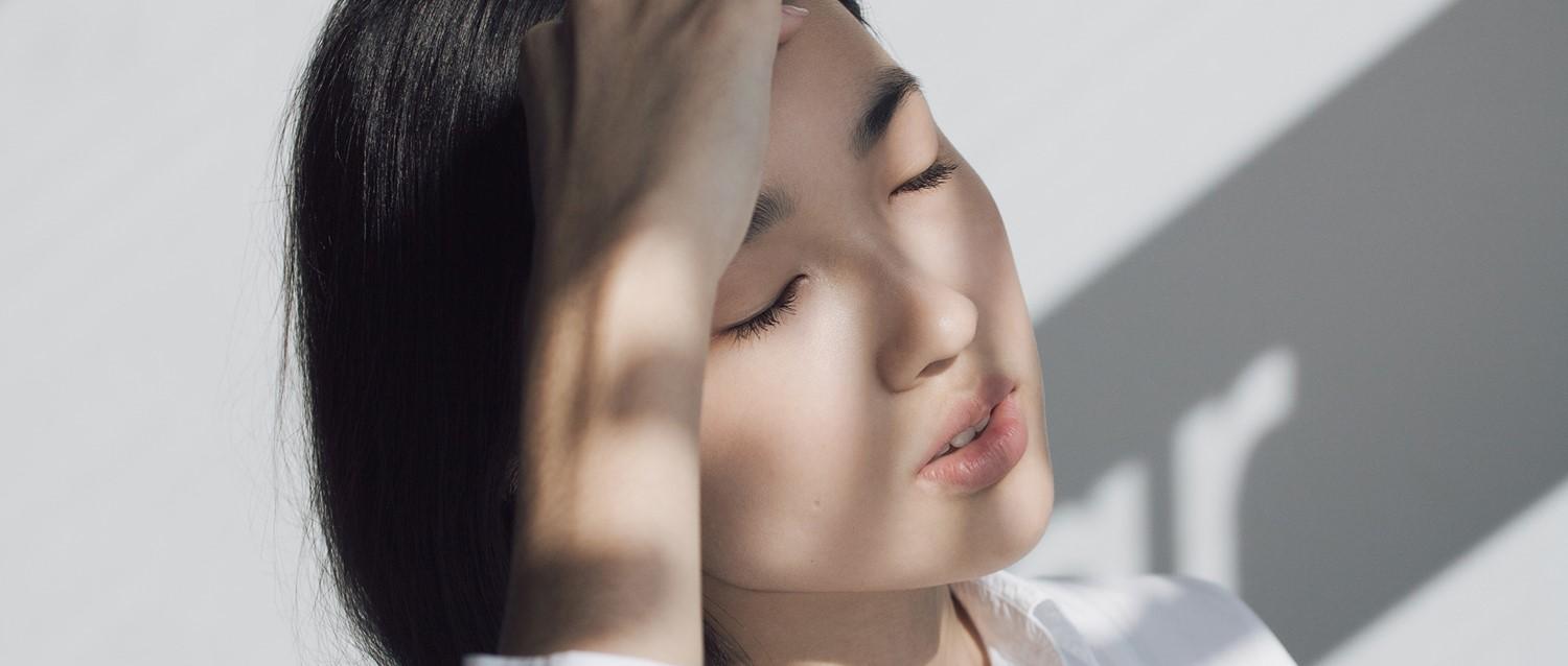 Personne aux cheveux noirs et aux yeux fermés sous un éclairage doux, les ombres créant une atmosphère sereine et paisible.