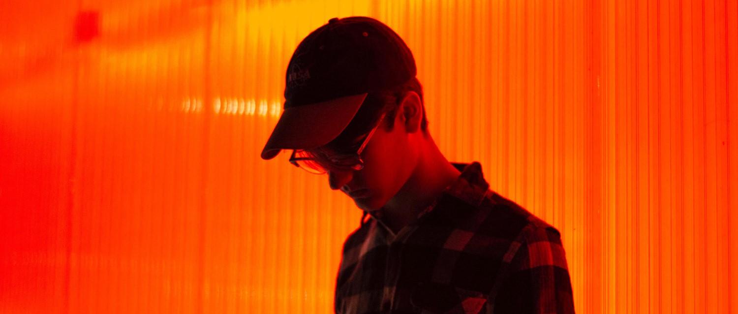Silhouette d'une personne portant une casquette et des lunettes sur un fond orange vibrant avec des stries lumineuses verticales.