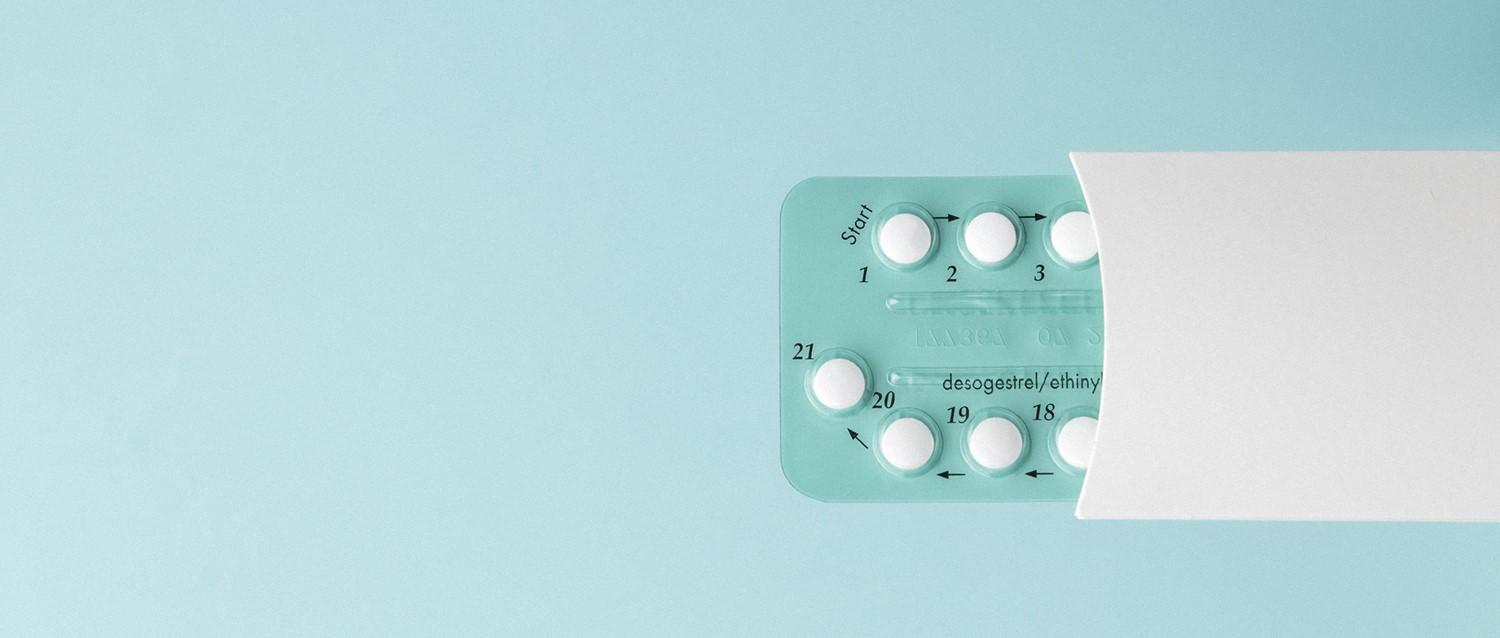 Emballage de pilules contraceptives montrant des comprimés blancs numérotés dans une plaquette thermoformée sarcelle sur un fond bleu clair.