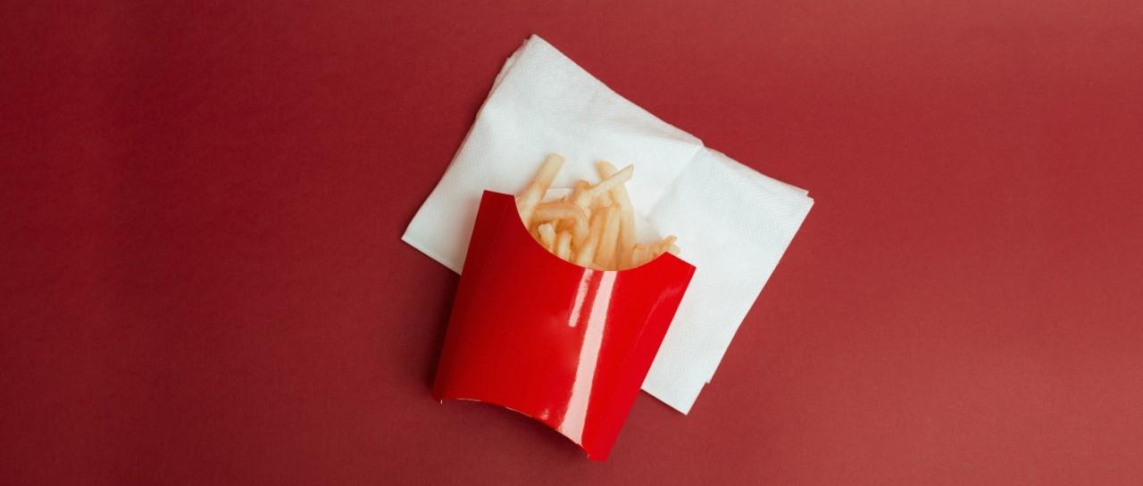 Frites dans une boîte en carton rouge sur une serviette blanche sur fond rouge.