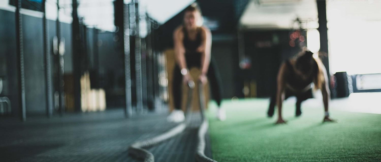 Des silhouettes floues font de l'exercice dans une salle de sport moderne au sol vert, en se concentrant sur la musculation dans un cadre sombre.