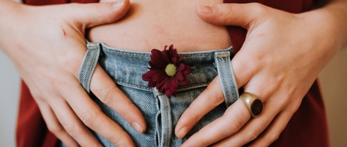 Mains formant un cœur sur une ceinture en denim avec une petite fleur bordeaux intégrée, la personne portant une bague.