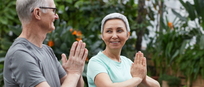Couple de seniors pratiquant le yoga en plein air, prenant la pose de la prière avec les mains jointes sur un fond vert luxuriant.