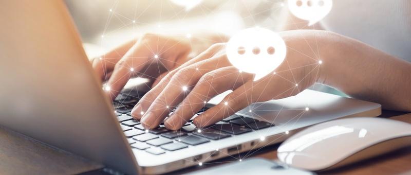 Mains tapant sur le clavier d'un ordinateur portable avec, en surimpression, des bulles de dialogue numérique et des points de connexion au réseau, suggérant une communication en ligne.