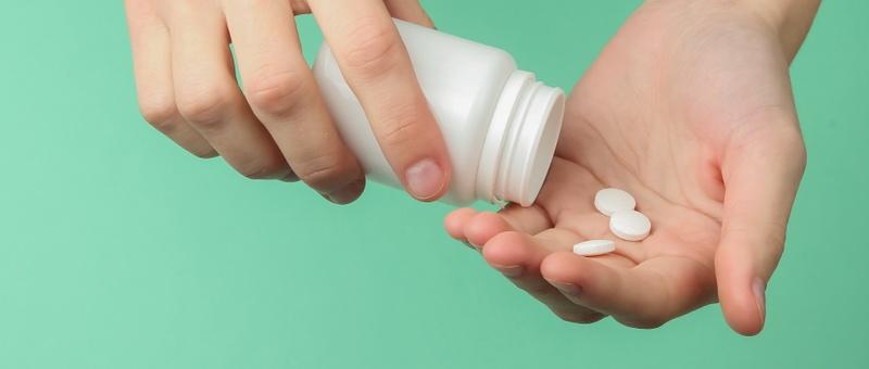 Pair of Caucasian hands holding white medicine bottle, and shaking out contents into palm.